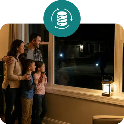 A family of four standing by a window looking out at a dark, unlit neighborhood during a power outage, while their own home remains warm and lit by battery backup power.